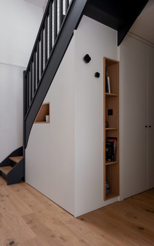 Mobilier sur mesure sous escalier avec façades blanches et niches en bois intégrées pour optimiser le rangement dans une entrée
