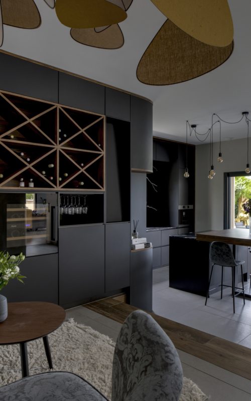 Vue de la cuisine noire avec cave à vin encastrée dans un projet de création cuisine et cave à vin à Pommiers, incluant un îlot central, un meuble vitrine et un coin repas ouvert sur l’extérieur